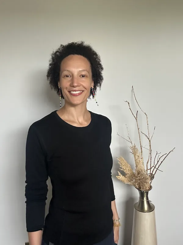 Portrait of Living Well Studios Practioner Bree, LMT stands in front of a neutral wall with her natural afro and smiling at the camera 