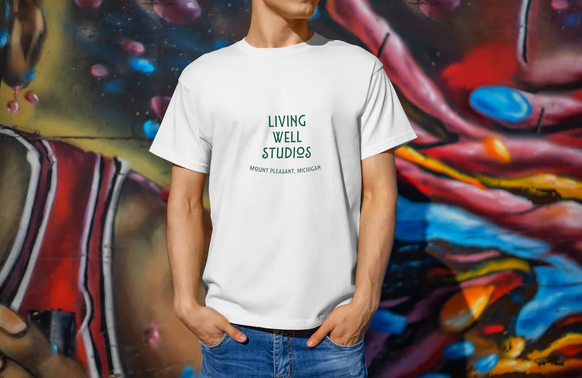 A man against a colorful wall wearing a light colored Living Well Studios original logo T-shirt